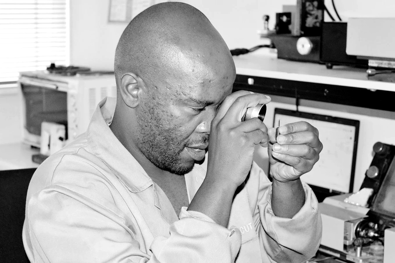 A Procut DCW diamond cutter inspecting a polished diamond through a loupe held in tweezers, Bedfordview workshop
